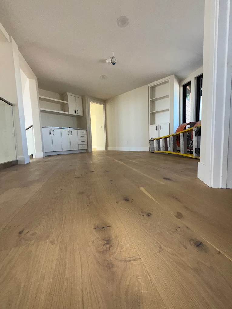 A freshly installed wide plank oak floor in an empty room, photographed during finishing