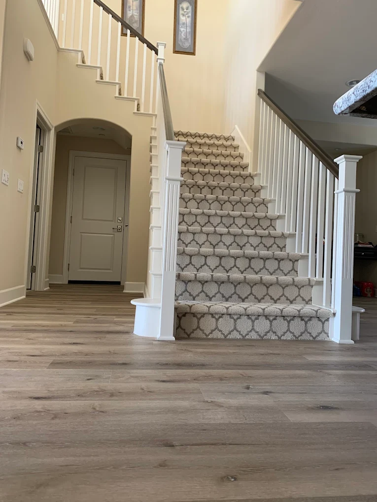Staircase fitted with a patterned grey and cream carpet runner, above a grey wood-look plank floor